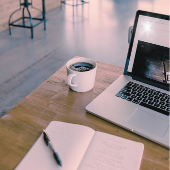 Espresso cup on a table next to a laptop and a pen and paper